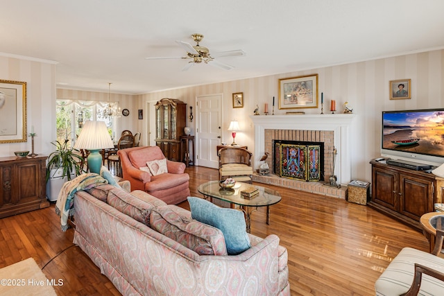 living area featuring ornamental molding, a fireplace, wallpapered walls, and wood finished floors