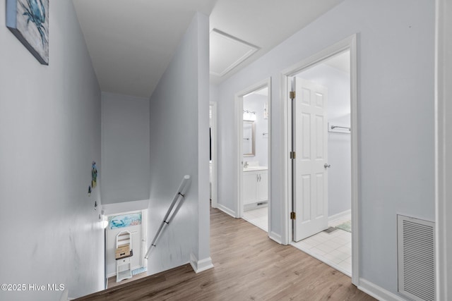 corridor featuring an upstairs landing, visible vents, baseboards, and wood finished floors