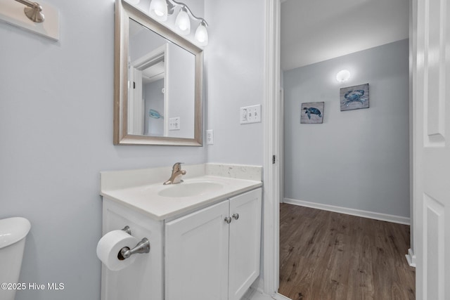 half bathroom featuring vanity, toilet, wood finished floors, and baseboards