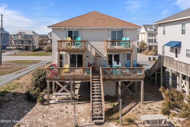 rear view of property with stairway, a balcony, and roof with shingles