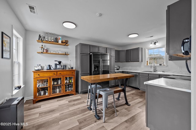 kitchen with a sink, stainless steel dishwasher, gray cabinetry, and light countertops