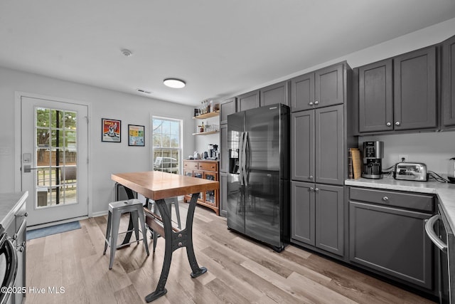 kitchen with a wealth of natural light, gray cabinetry, light wood-style flooring, stainless steel refrigerator with ice dispenser, and light countertops