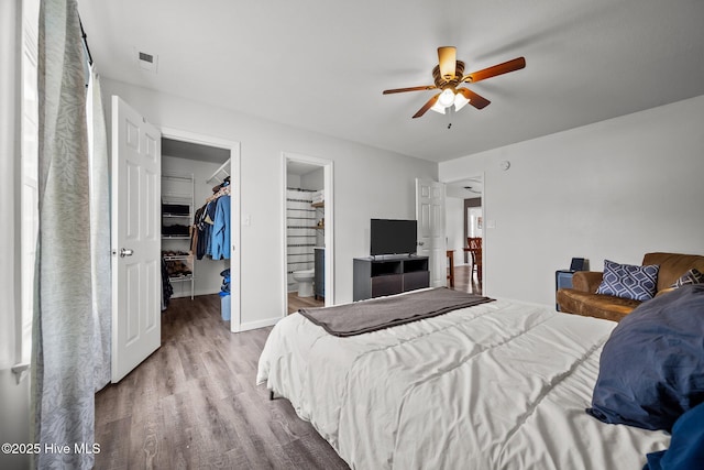 bedroom with a spacious closet, visible vents, ensuite bathroom, wood finished floors, and a closet