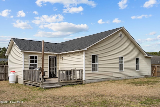 rear view of house with a lawn, a wooden deck, and fence