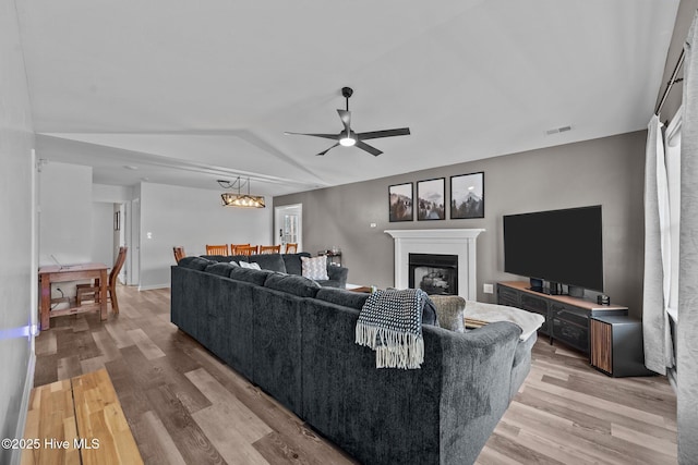 living room featuring visible vents, vaulted ceiling, light wood-style flooring, ceiling fan with notable chandelier, and a glass covered fireplace