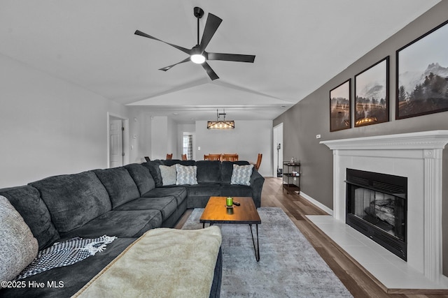 living room with baseboards, a tiled fireplace, lofted ceiling, wood finished floors, and a ceiling fan