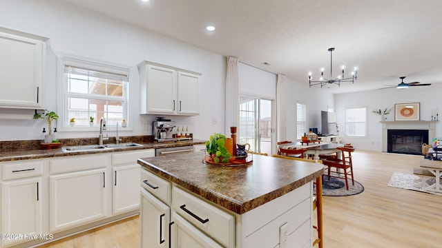 kitchen featuring ceiling fan with notable chandelier, a sink, dark countertops, open floor plan, and a glass covered fireplace