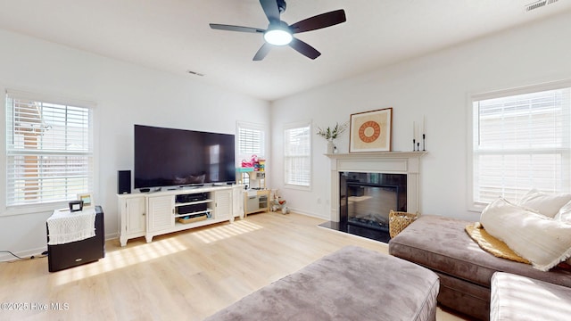 living area featuring visible vents, a fireplace with flush hearth, light wood finished floors, baseboards, and ceiling fan