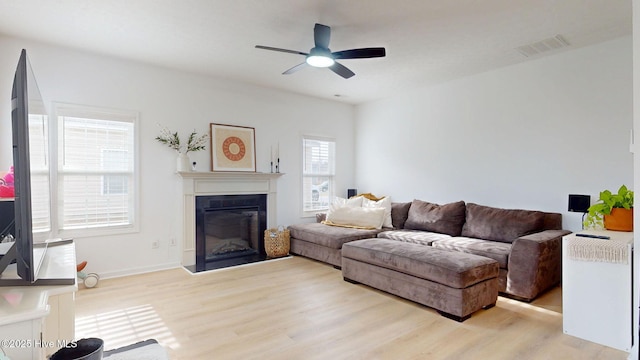 living room featuring a glass covered fireplace, visible vents, wood finished floors, and a ceiling fan