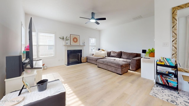 living area featuring a glass covered fireplace, visible vents, ceiling fan, and wood finished floors