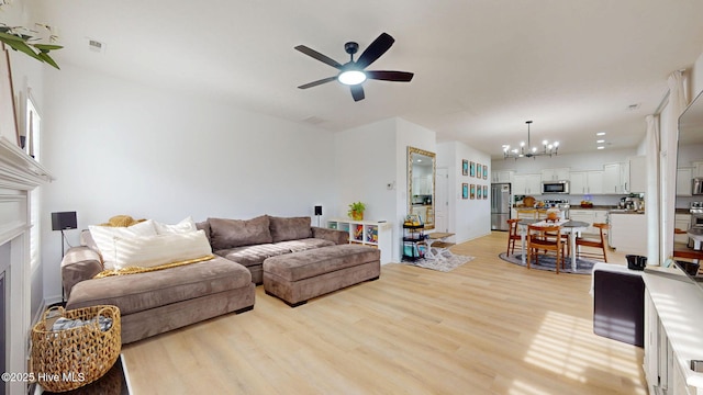 living room with a fireplace, ceiling fan with notable chandelier, visible vents, and light wood finished floors