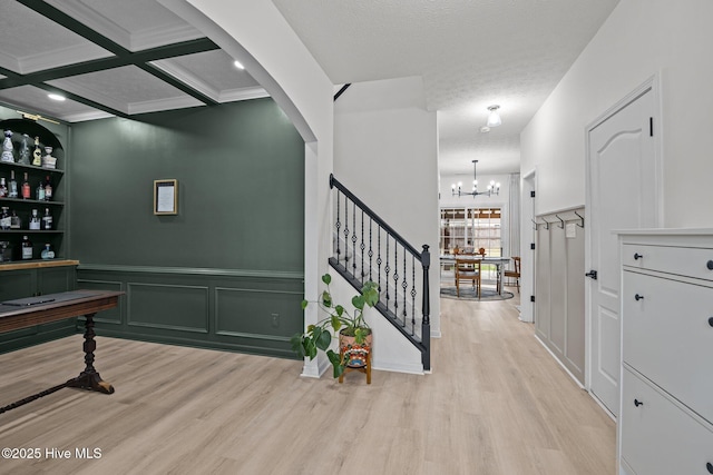 interior space with light wood-type flooring, coffered ceiling, stairs, and a decorative wall