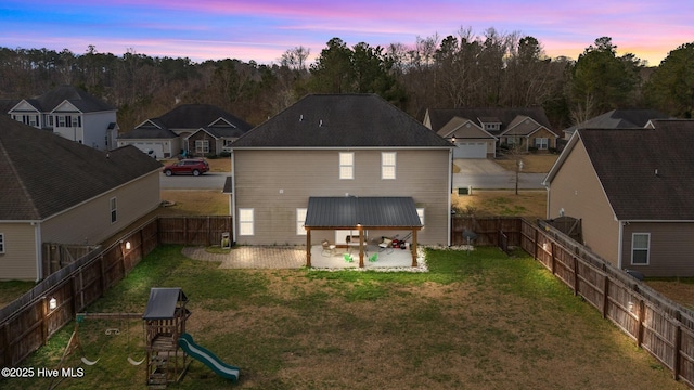 back of property at dusk featuring a playground, a yard, a patio area, and a fenced backyard