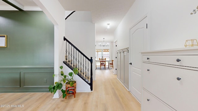 corridor with a chandelier, stairway, a decorative wall, and light wood-type flooring