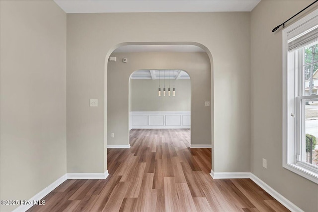 hallway featuring baseboards, arched walkways, and wood finished floors