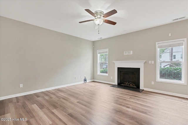 unfurnished living room featuring baseboards, wood finished floors, visible vents, and a fireplace with raised hearth