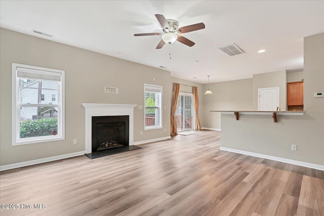 unfurnished living room with visible vents, a fireplace with raised hearth, baseboards, and light wood-style floors