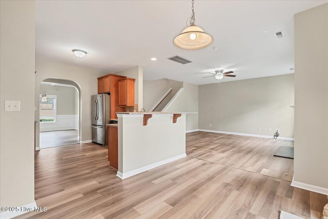 kitchen featuring visible vents, arched walkways, freestanding refrigerator, a kitchen breakfast bar, and brown cabinets