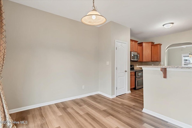 kitchen featuring arched walkways, appliances with stainless steel finishes, light wood-type flooring, and baseboards