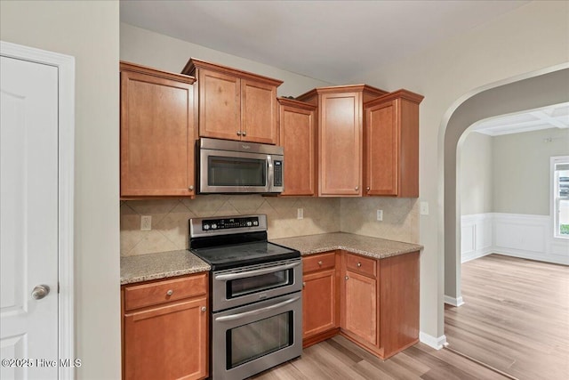 kitchen with tasteful backsplash, arched walkways, light wood-style floors, appliances with stainless steel finishes, and light stone countertops