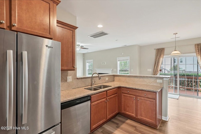 kitchen featuring visible vents, a peninsula, a sink, stainless steel appliances, and brown cabinets