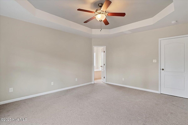 empty room with a tray ceiling, a ceiling fan, baseboards, and carpet floors