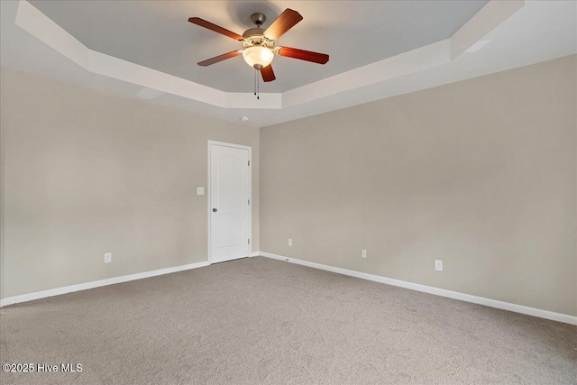 empty room with a tray ceiling, baseboards, carpet floors, and ceiling fan