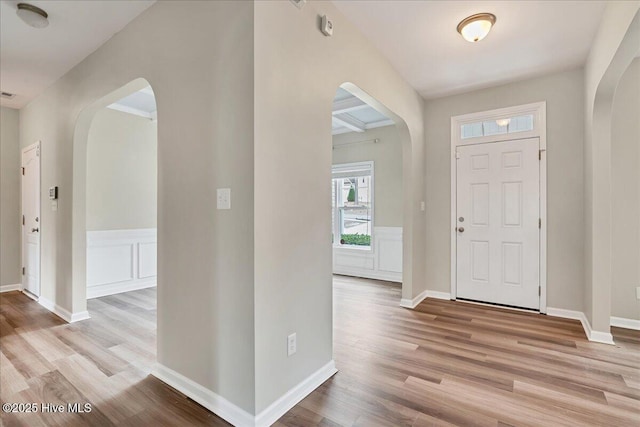 foyer with arched walkways, a wainscoted wall, and wood finished floors