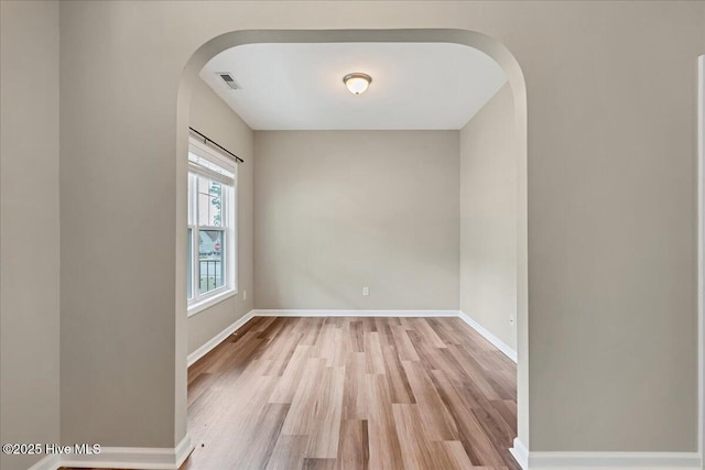 empty room featuring baseboards, visible vents, light wood finished floors, and arched walkways