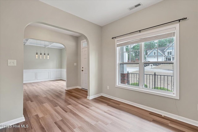 spare room featuring visible vents, arched walkways, baseboards, and wood finished floors