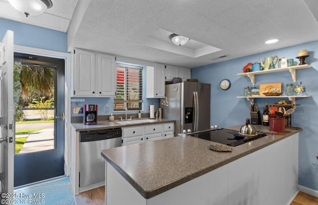 kitchen with a sink, appliances with stainless steel finishes, a peninsula, white cabinets, and open shelves