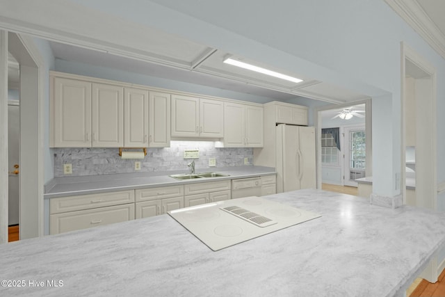 kitchen with white appliances, a sink, decorative backsplash, light countertops, and crown molding