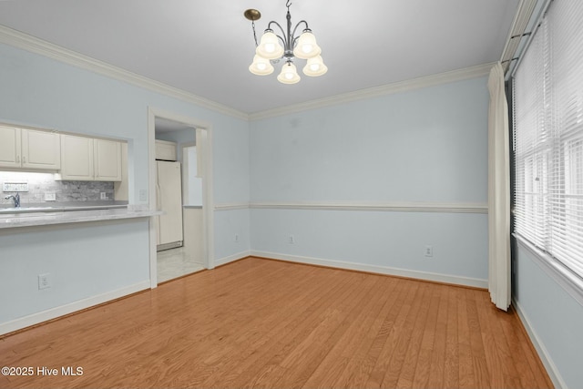 interior space featuring baseboards, light wood finished floors, a sink, crown molding, and a chandelier