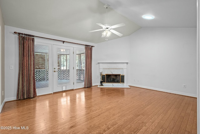 unfurnished living room featuring a ceiling fan, wood finished floors, baseboards, a high end fireplace, and vaulted ceiling