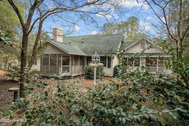 back of property with a shingled roof, a chimney, and a sunroom