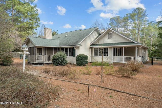 rear view of house featuring a shingled roof, fence, covered porch, a sunroom, and a chimney