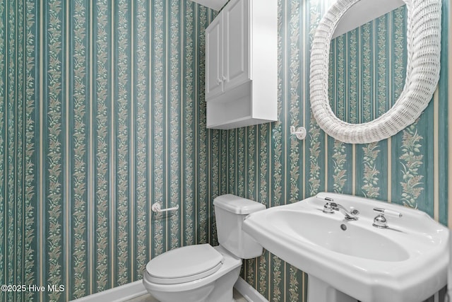 bathroom with toilet, wallpapered walls, and a sink