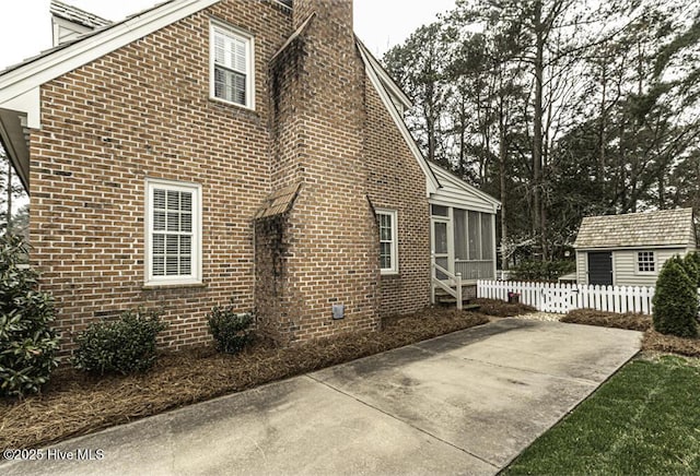 view of property exterior featuring fence, brick siding, a sunroom, and a chimney