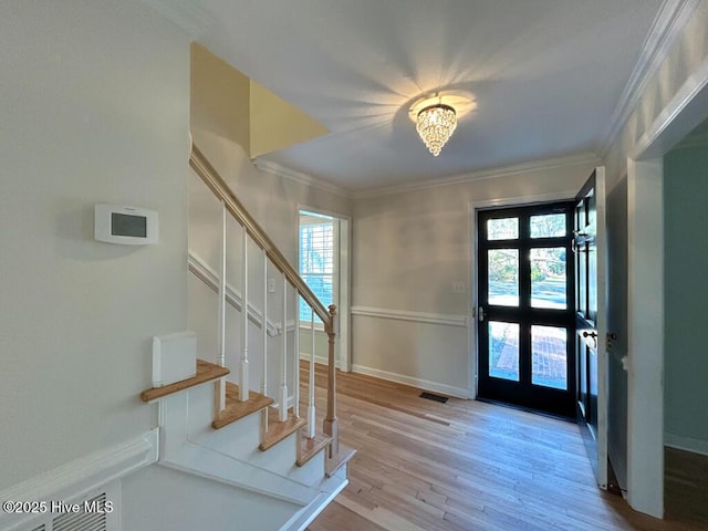 entryway featuring wood finished floors, baseboards, visible vents, ornamental molding, and stairs