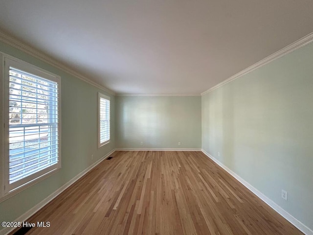 spare room featuring light wood finished floors, visible vents, baseboards, and ornamental molding