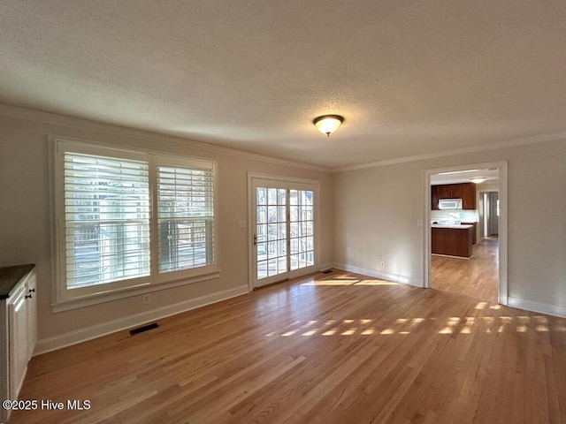 interior space featuring crown molding, visible vents, light wood finished floors, and a textured ceiling