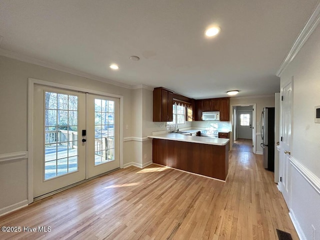 kitchen featuring white microwave, a peninsula, freestanding refrigerator, a sink, and light countertops