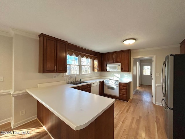 kitchen featuring a healthy amount of sunlight, light wood-type flooring, a peninsula, white appliances, and a sink