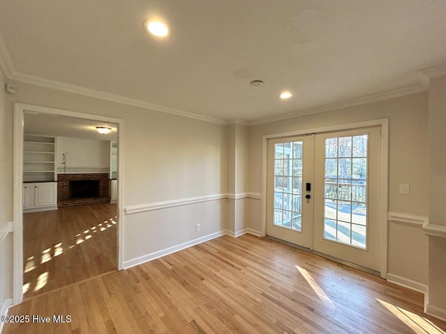 interior space with baseboards, ornamental molding, french doors, a fireplace, and wood finished floors