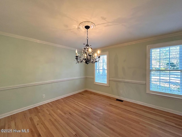 spare room with baseboards, an inviting chandelier, wood finished floors, and crown molding