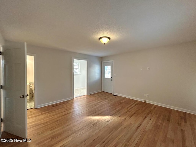 spare room with baseboards, light wood finished floors, and a textured ceiling