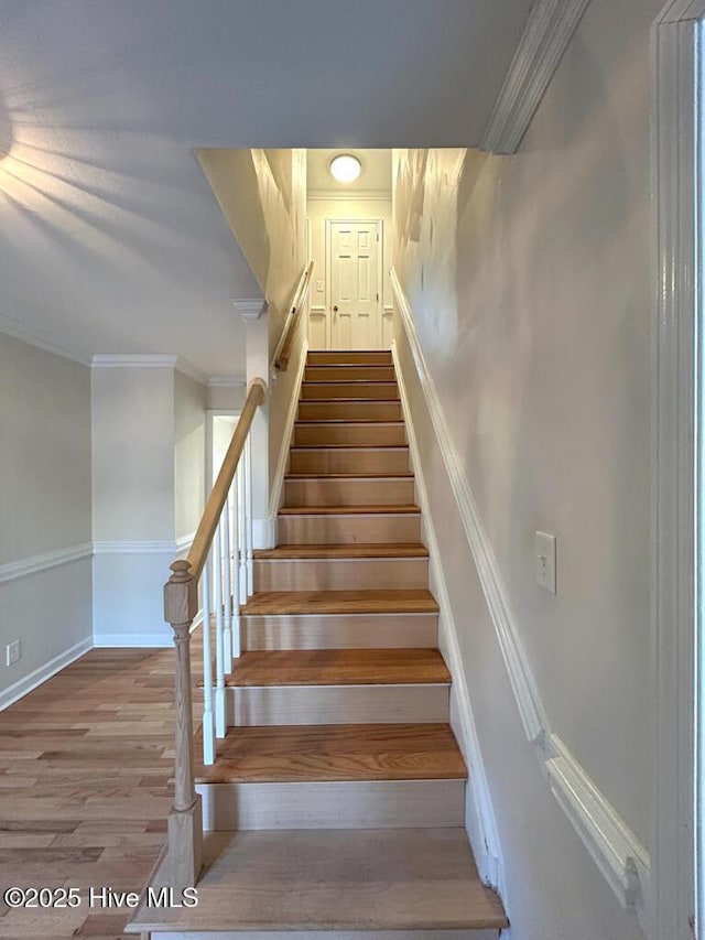 staircase featuring crown molding, baseboards, and wood finished floors