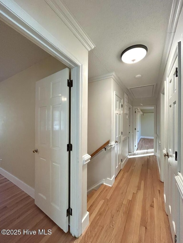 hallway featuring crown molding, baseboards, attic access, light wood-style floors, and a textured ceiling