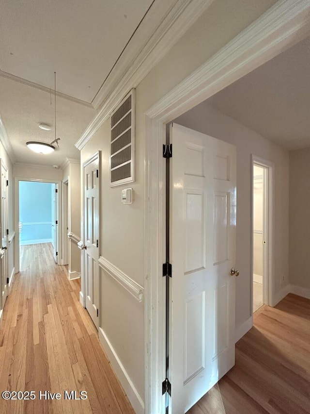 hallway with visible vents, crown molding, baseboards, attic access, and light wood-type flooring