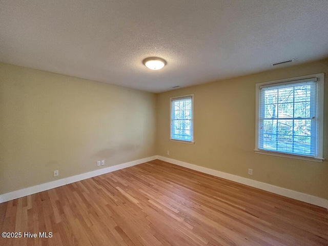 empty room featuring baseboards, visible vents, a textured ceiling, and light wood-style floors